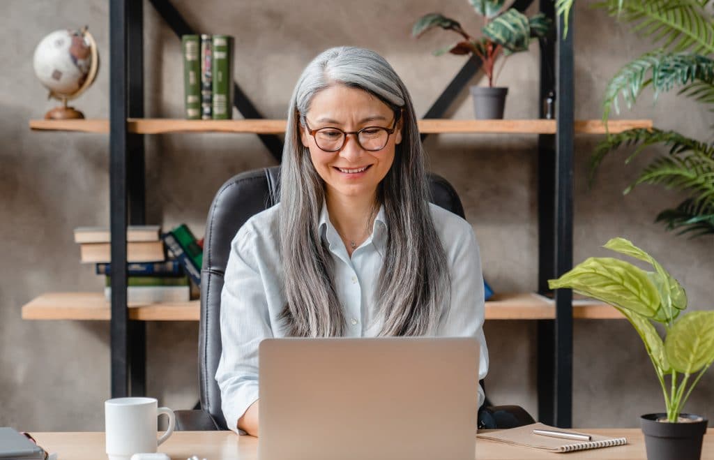 Pretty grey-haired mature woman working in a cosy office using laptop