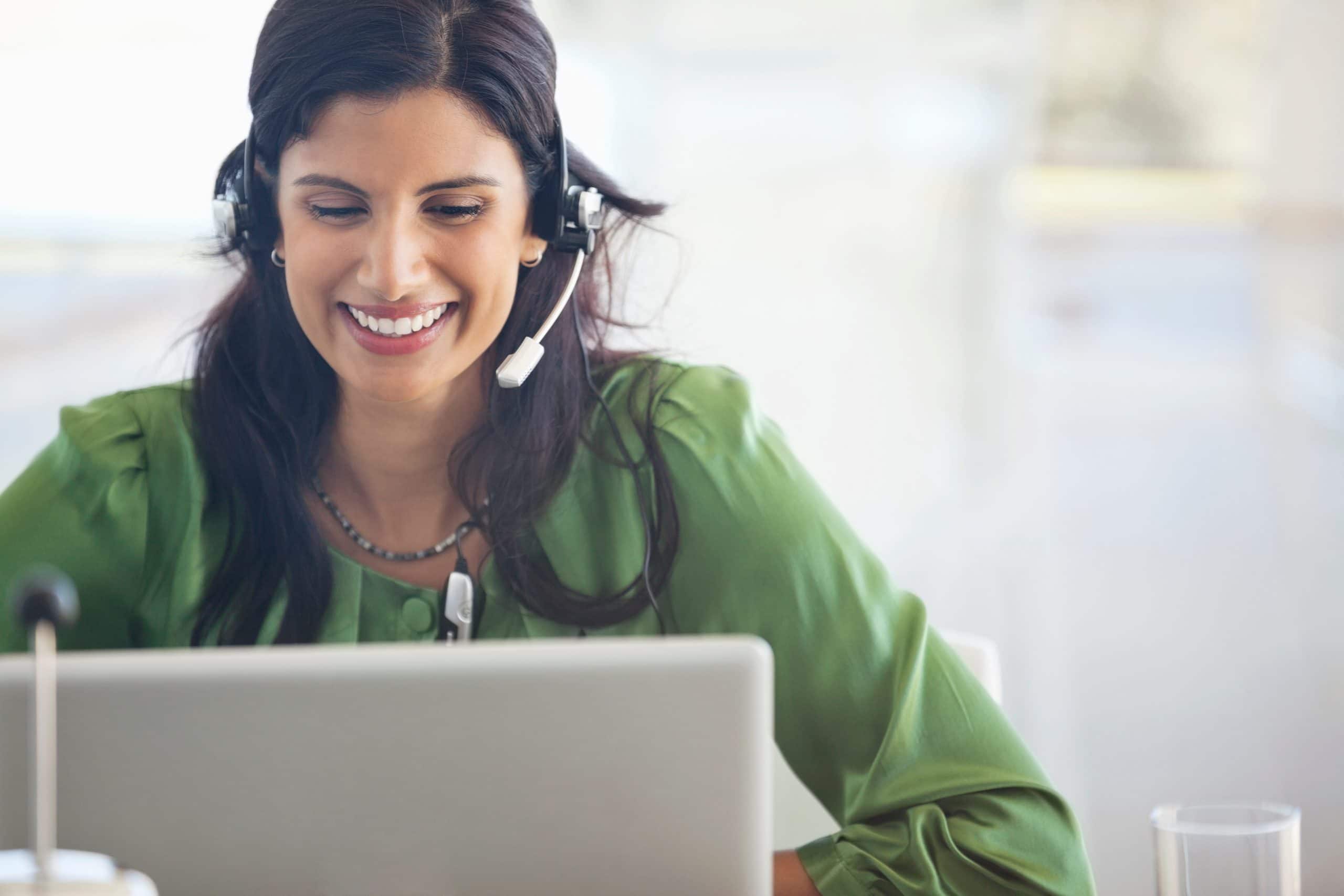 Businesswoman in green blouse, wearing headset at desk