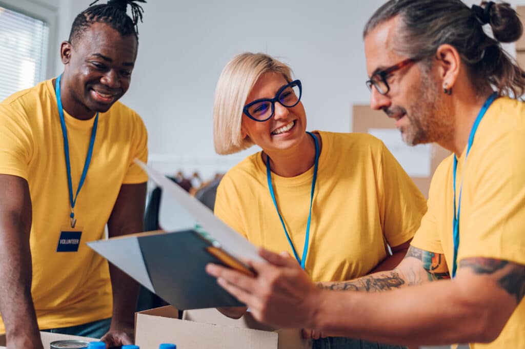 Three nonprofit board members wearing yellow shirts, smiling and looking at documents together.